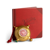 A gold ornament that looks a bit like a compass on a red hanger. There is a QR code in the center to scan for videos, displayed next to a red bound journal that says "Santa's Kindness Journal".