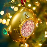 A gold plastic compass shaped ornament with a QR code in the center hanging on a lit Christmas tree.