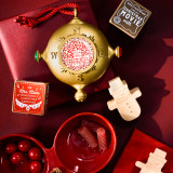 The Santa Kindness ornament and journal on a red background with other holiday products such as a dice game and red serving dish.